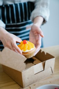 Close-up of a gourmet fruit-topped cupcake being placed in a carton box.
